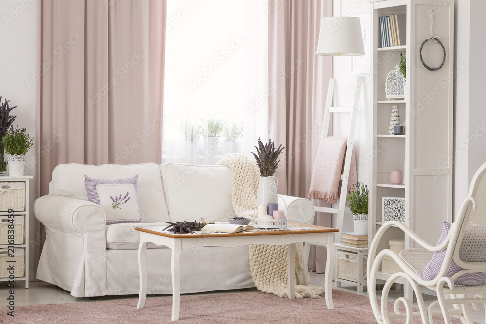 白色沙发旁的木质桌子，粉色客厅内部有窗帘和植物。真实照片