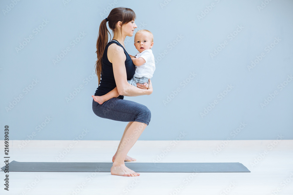 运动、母性和积极的生活方式理念——年轻母亲与蹒跚学步的孩子一起做瑜伽的侧视图