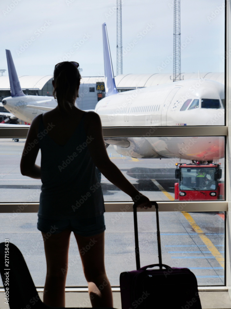 SILHOUETTE: Woman grabs her luggage and looks through the window at airplane.
