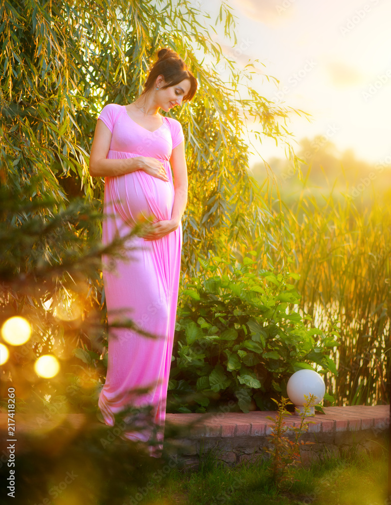怀孕的快乐女人在夏季公园抚摸她的肚子。全身孕妇美女户外p