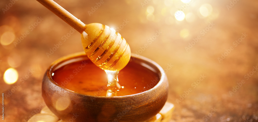 蜂蜜。健康的有机稠蜂蜜从木碗中的蜂蜜勺中滴下。甜甜点回来了
