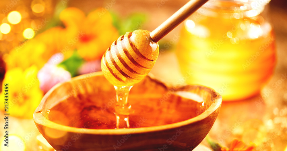 蜂蜜。健康的有机稠蜂蜜从木碗里的蜂蜜勺里滴下来。甜甜点回来了