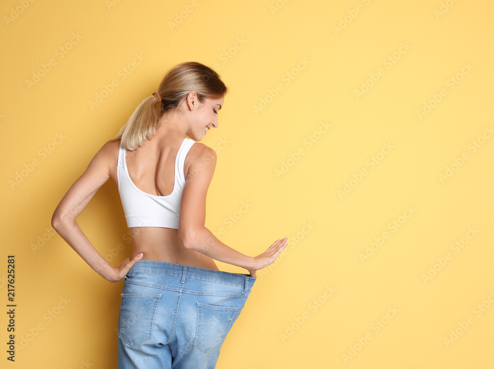 穿着旧大牛仔裤的年轻苗条女性在彩色背景下展示她的饮食效果