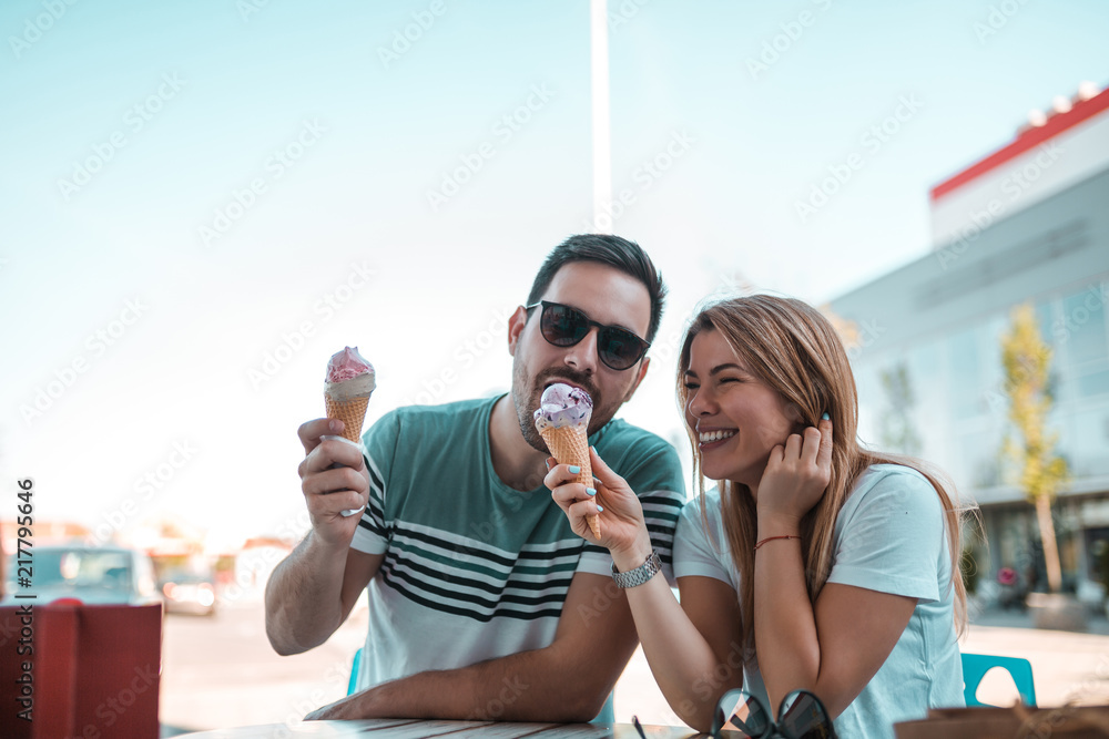 英俊的年轻人坐在户外，一边吃着他的女朋友们的冰淇淋，一边玩得很开心。