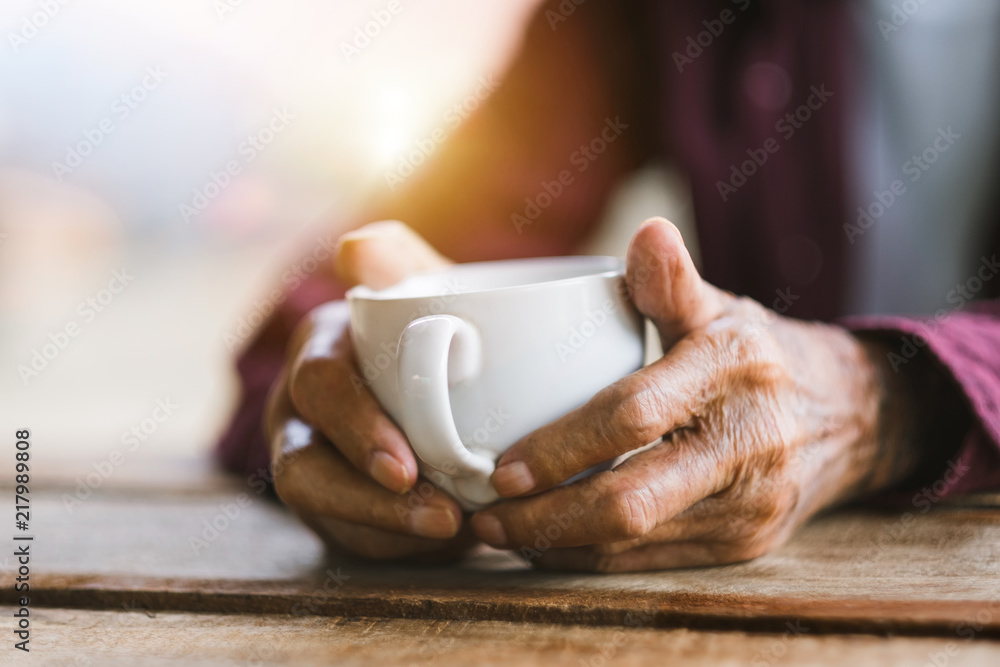 木头桌子上拿着一杯咖啡的老人的手。语调