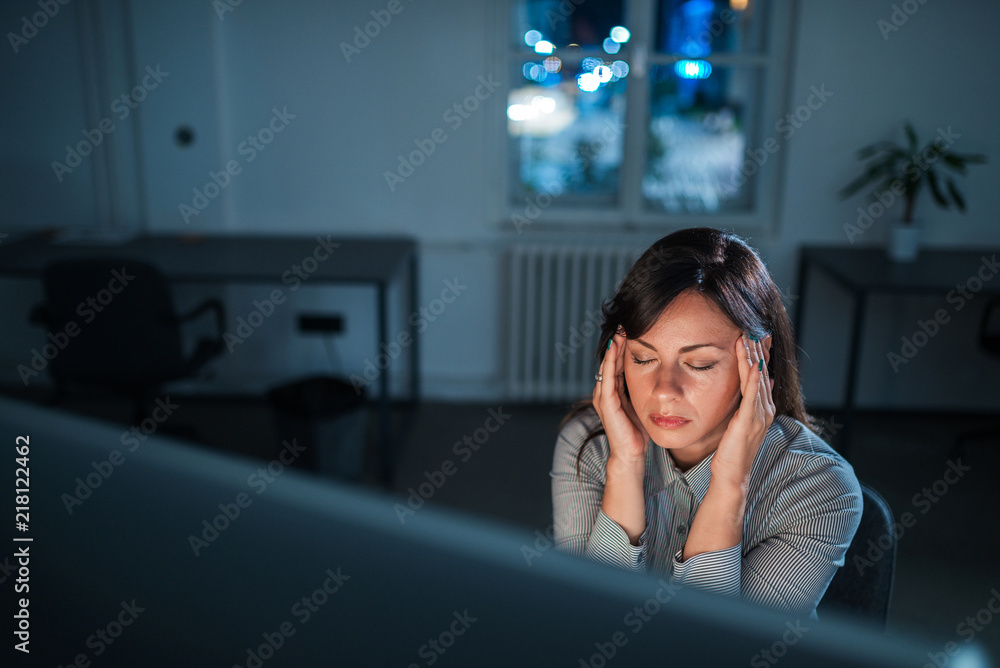 晚上坐在电脑屏幕前疲惫疲惫的年轻女子。