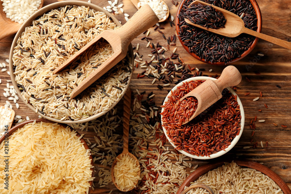 Different types of rice in bowls on wooden table