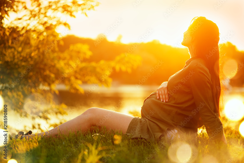 孕妇坐在夏日公园的绿草上，享受大自然。健康怀孕理念