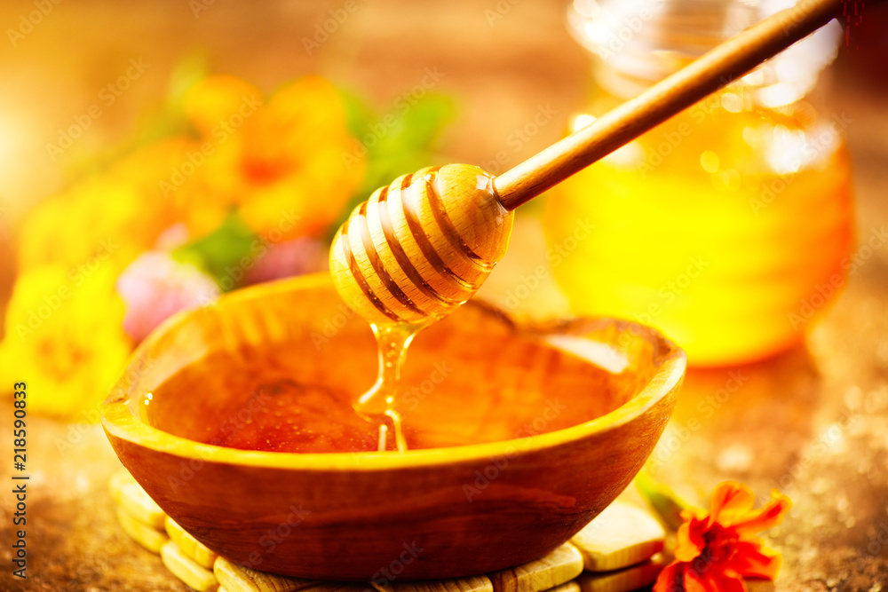 蜂蜜从木碗中的蜂蜜勺中滴下。健康的有机稠蜂蜜从木盆中倒出