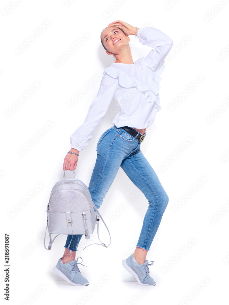 美女时尚模特女孩穿着牛仔裤和运动鞋，背着时尚的银色背包摆姿势