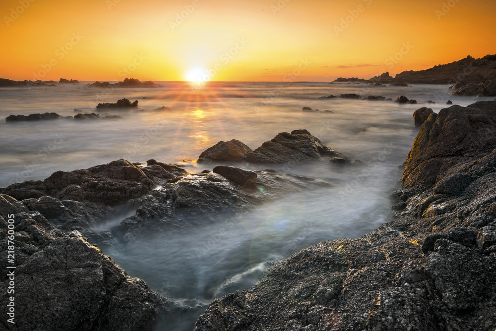 岩石海岸和柔软如丝的海水上的浪漫日落
