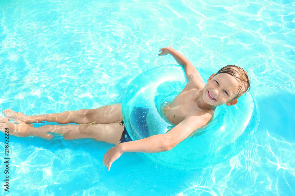 可爱的小男孩带着充气环在游泳池游泳
