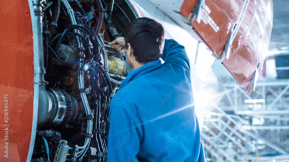 Aircraft maintenance mechanic inspects and tunes plane engine in a hangar.