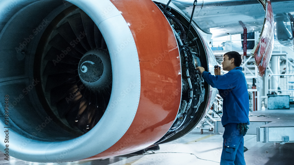 飞机维修机械师在机库里用闪光灯检查飞机发动机。