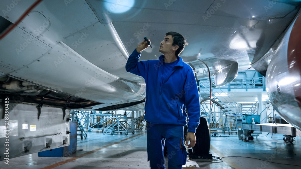 飞机维修机械师在机库里用闪光灯检查飞机机身。