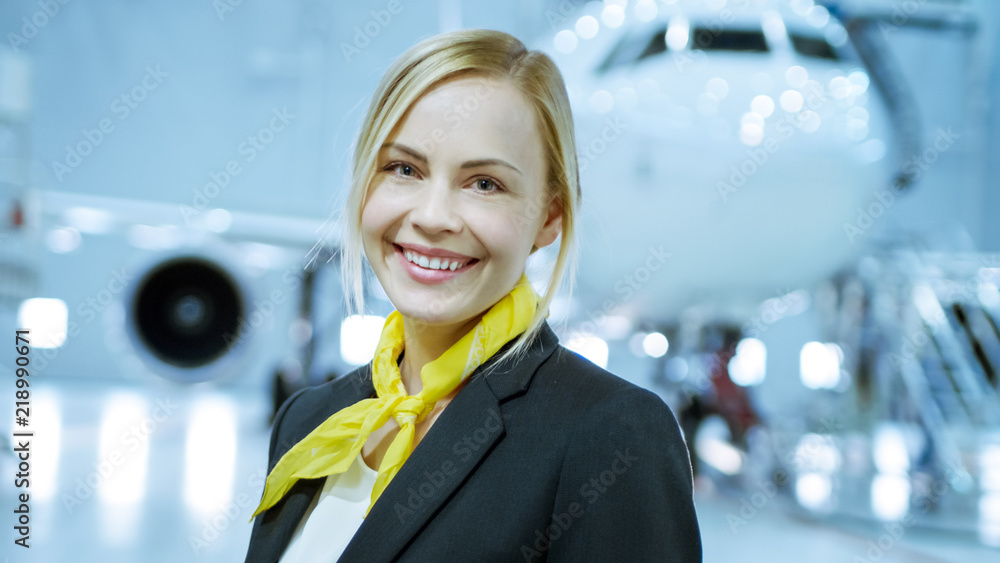 在飞机维修机库里，年轻漂亮的金发女乘务员/乘务员微笑迷人
