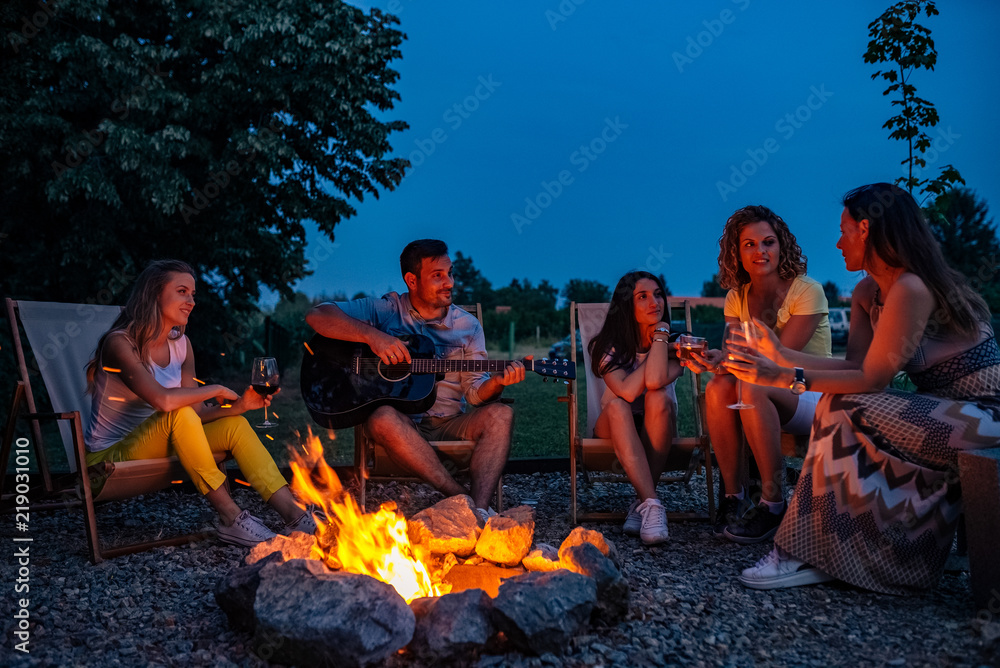 享受夏天。一个年轻人晚上在篝火旁为朋友弹吉他。