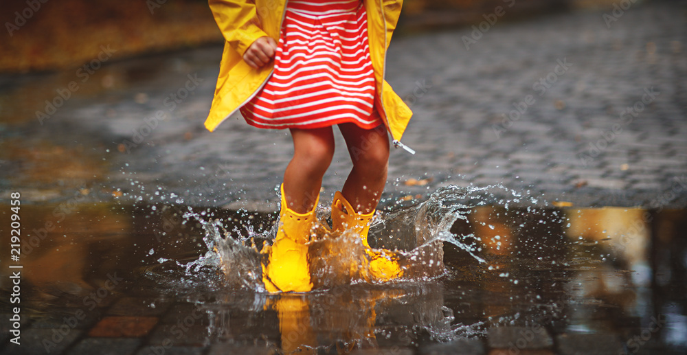 秋天散步时水坑里穿着橡胶靴的孩子的腿