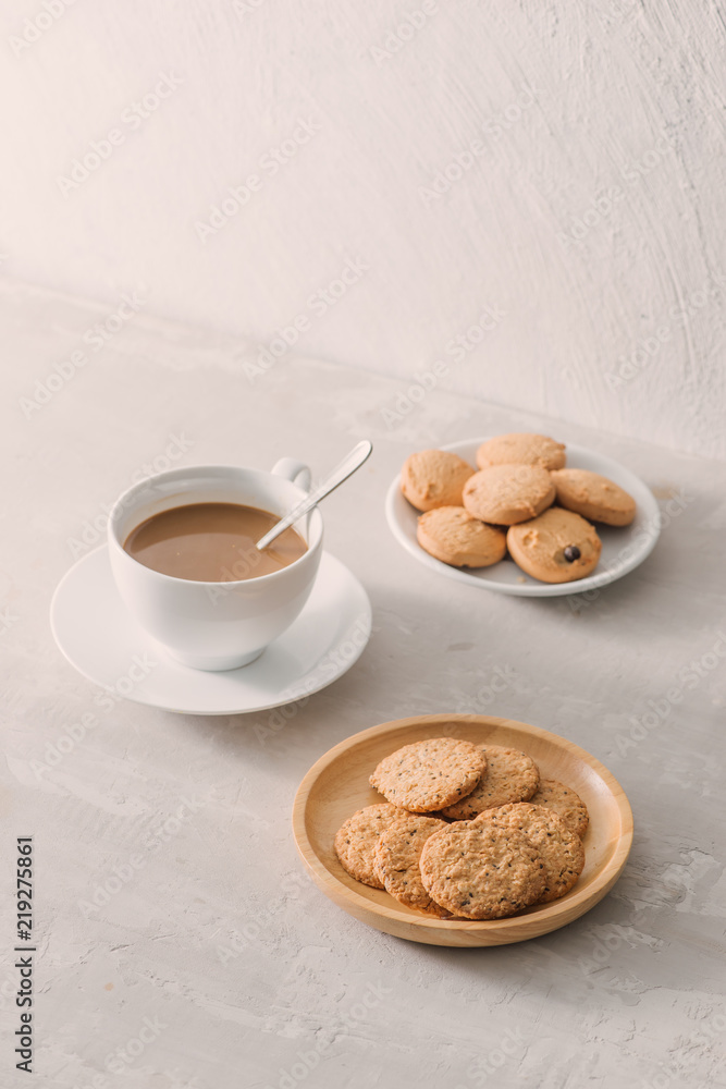 一杯咖啡配牛奶或卡布奇诺，配浅色石头背景的饼干。饮用时加入咖啡因或