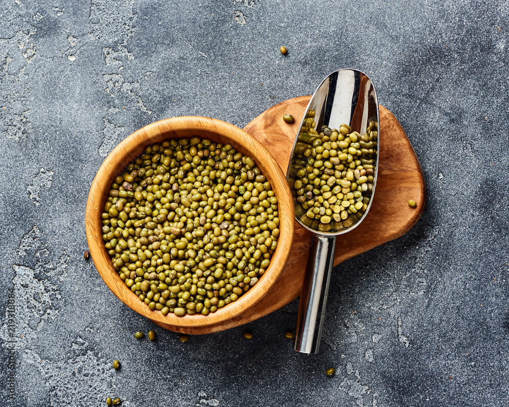 Green mung beans in wooden bowl on gray background. Top view of groats.