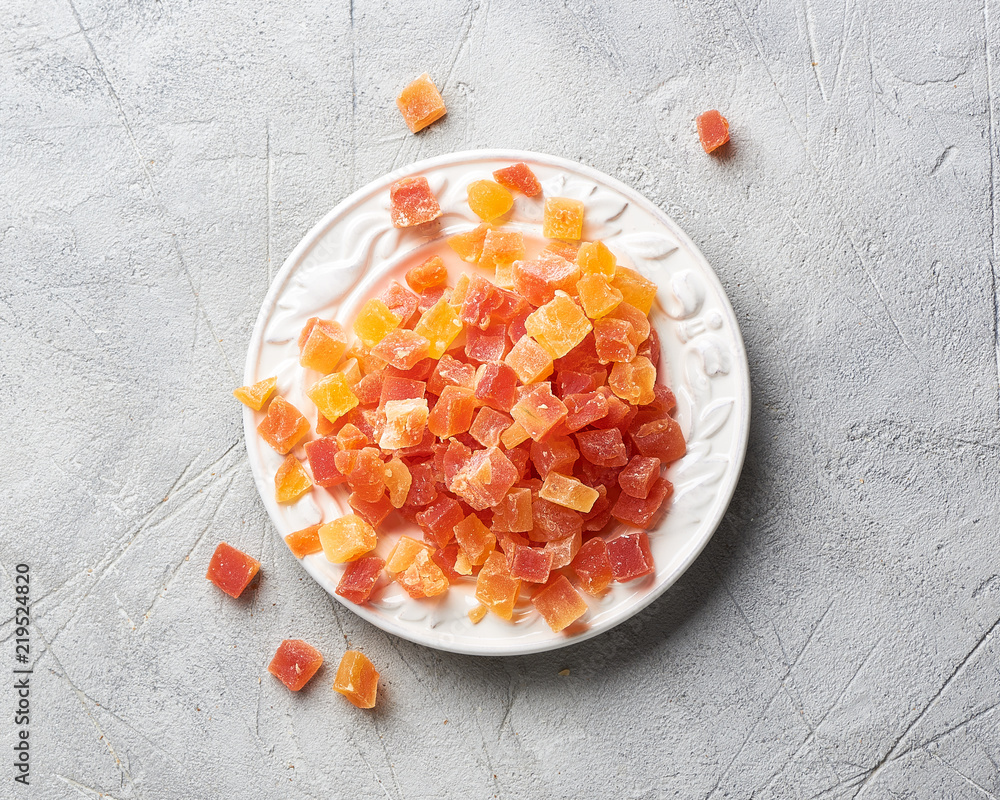 Cubes of dried apricot, mango and papaya on white plate. Candied fruits over gray background with co