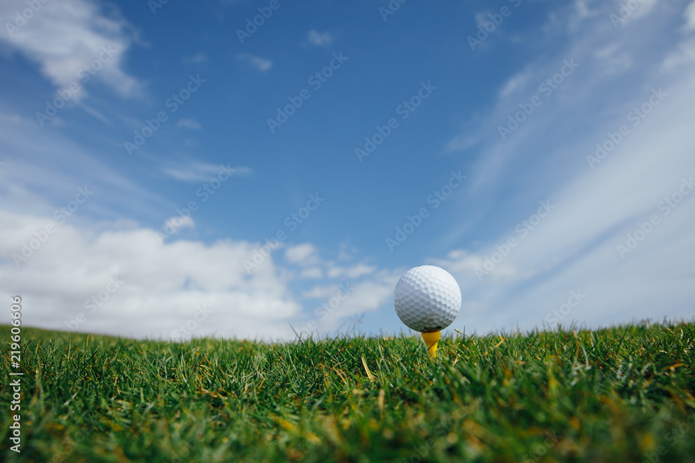 发球台上的高尔夫球，绿色的草地和蓝色的天空背景