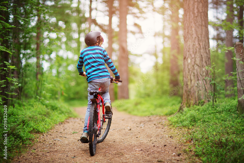清晨在森林里骑自行车的孩子。戴着头盔在户外骑行的男孩