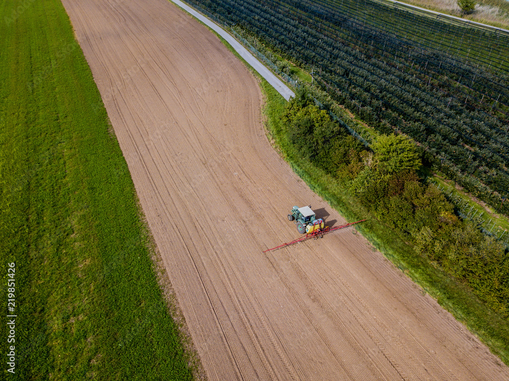 拖拉机在棕色土地上喷洒肥料的农田鸟瞰图。
