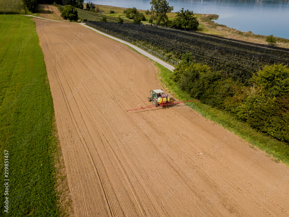 拖拉机在棕色土地上喷洒肥料的鸟瞰图。