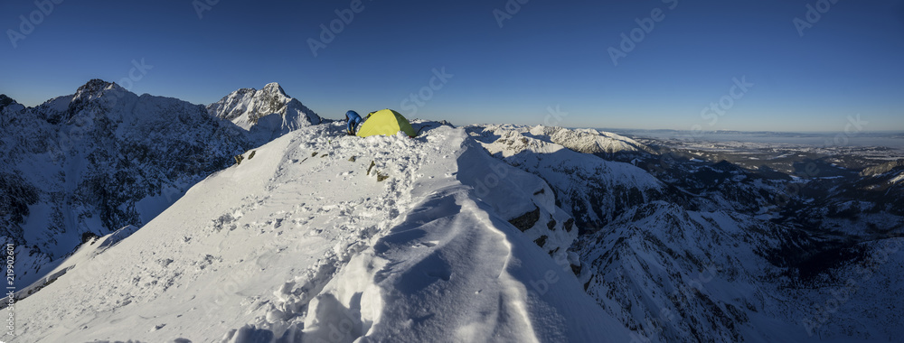黄色帐篷搭在高山的顶峰上。在白雪覆盖的山脉里露营。