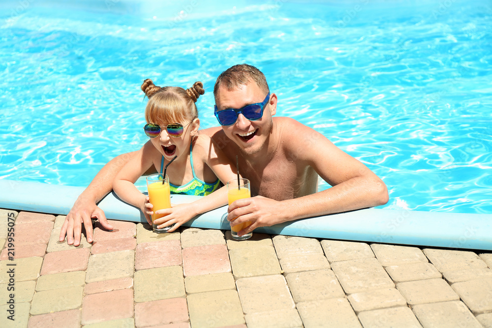 快乐的爸爸和女儿在游泳池里喝着果汁