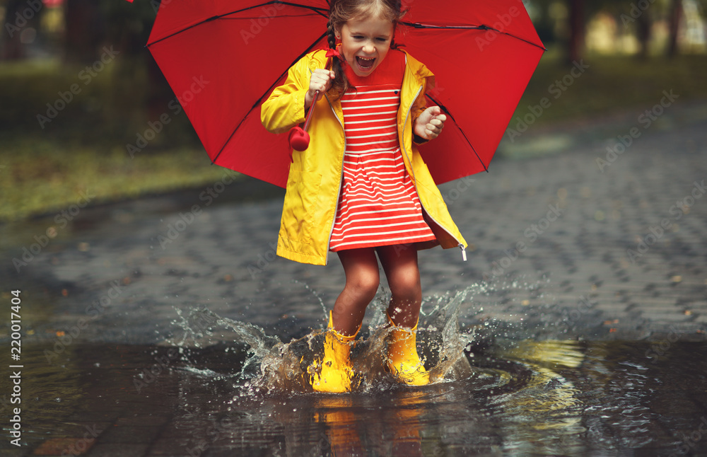 快乐的小女孩在秋天散步时，在水坑里撑着伞和橡胶靴