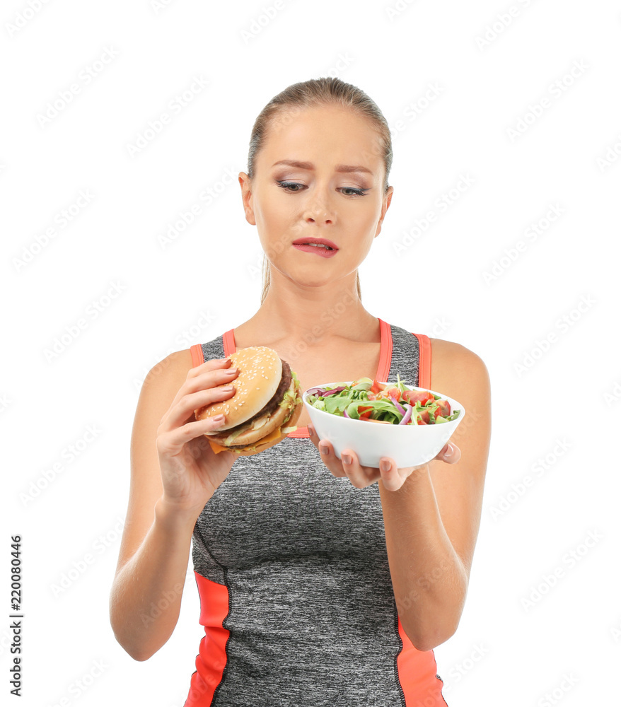 运动型女性在新鲜蔬菜沙拉和白底汉堡之间做出选择