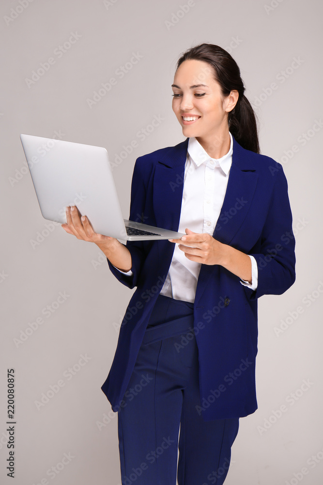 灰色背景下带笔记本电脑的漂亮女商人