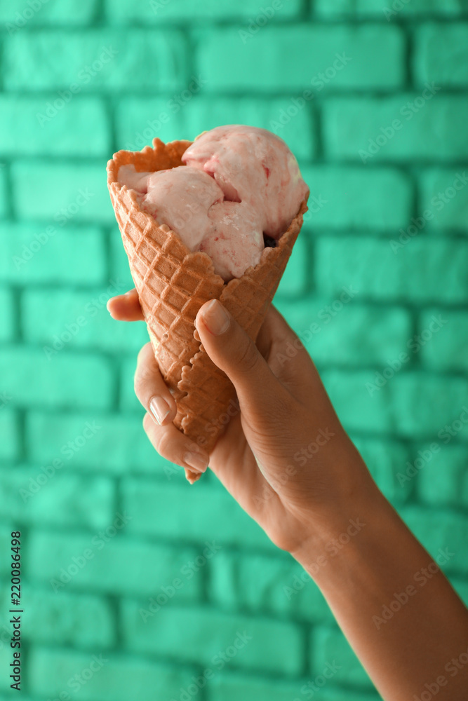 拿着华夫饼蛋卷和美味的草莓冰淇淋的女人靠着彩色砖墙