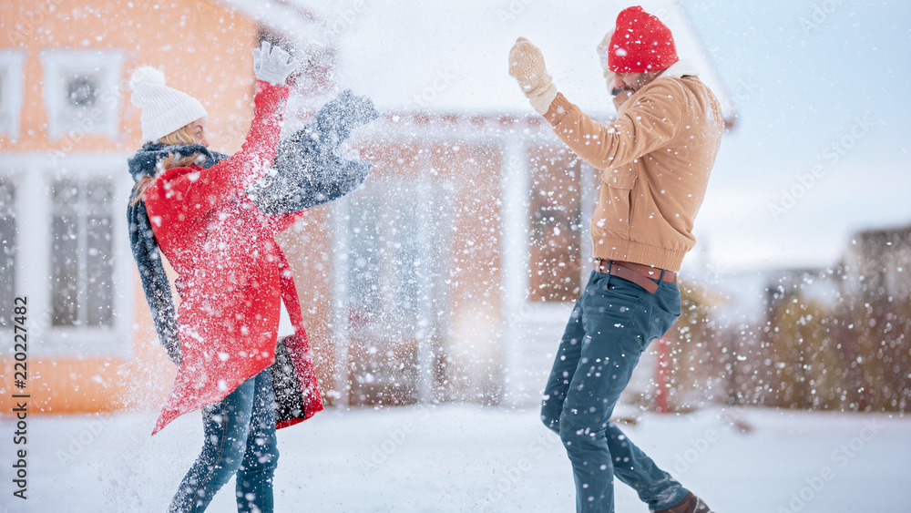 年轻夫妇顽皮地向空中扔雪，而冬季降雪仍在继续。快乐的男人和女人