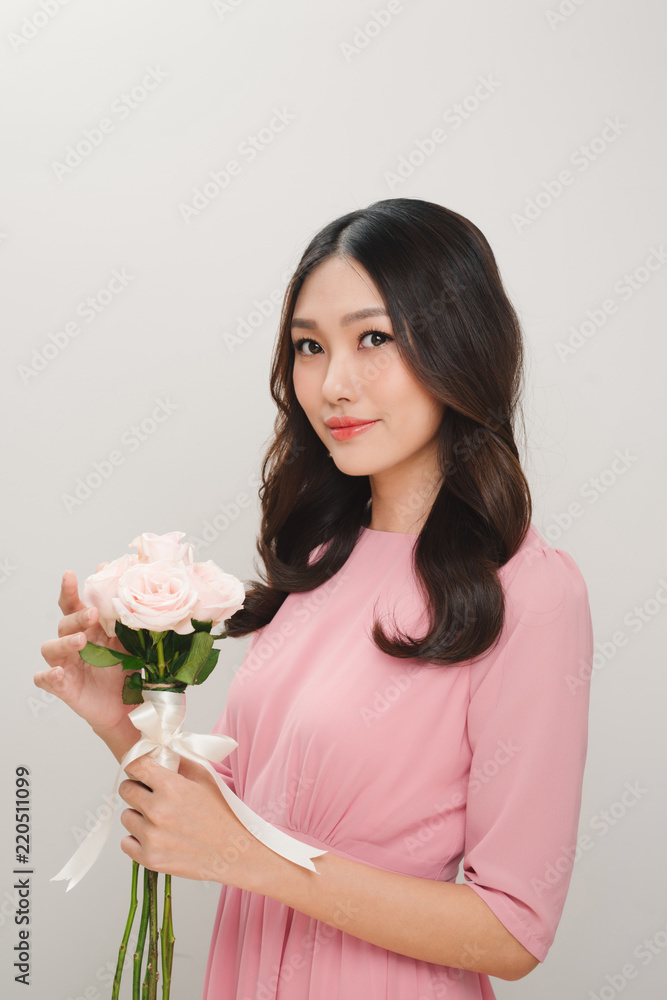 一位穿着粉色连衣裙的满意年轻女子的肖像，手里拿着一束孤立的玫瑰花