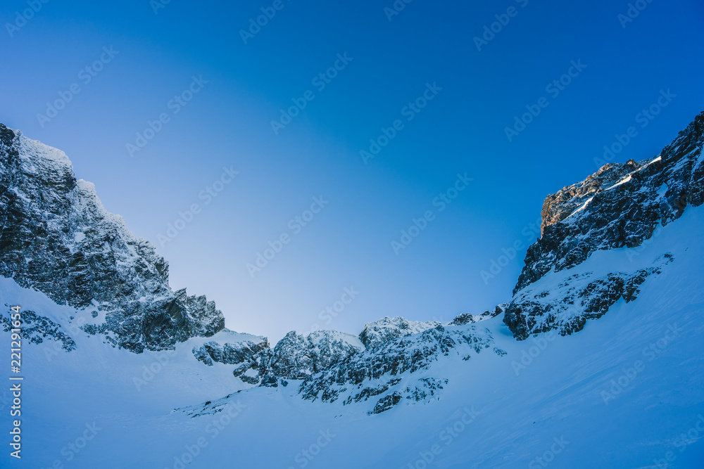 Background photo of a mountain valley, vibrant blue sky, mountain peaks, summits and rock ridke. Sno