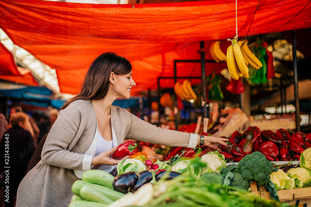兴高采烈的女人在农贸市场买新鲜蔬菜。
