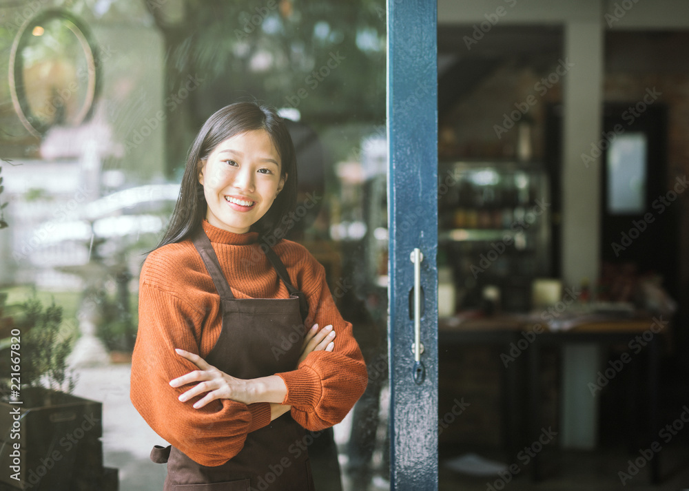 美丽的亚洲女店主站在咖啡店门口看着镜头