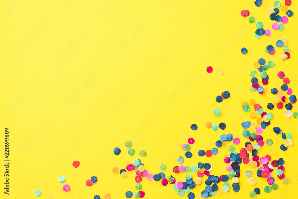 Flatlay of yellow background with colourful paper confetti in the corner and with copyspace