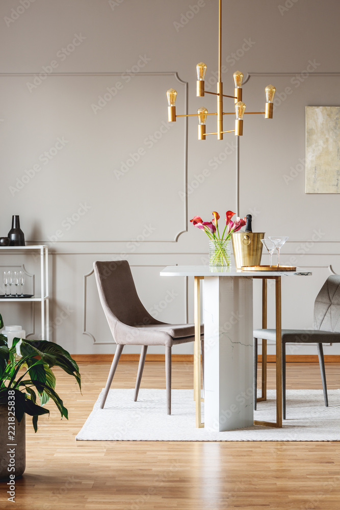 明亮的公寓内部有鲜花的餐桌上的椅子，配有植物和金色的灯。真正的phot