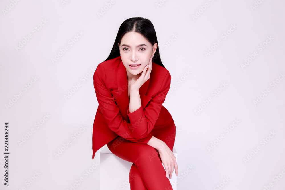 年轻自信的亚洲女性，身穿红色优雅西装，搭配裤子，半裸坐着
