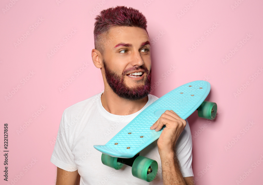 染头发、留胡子的英俊男子在彩色背景上拿着滑板的肖像