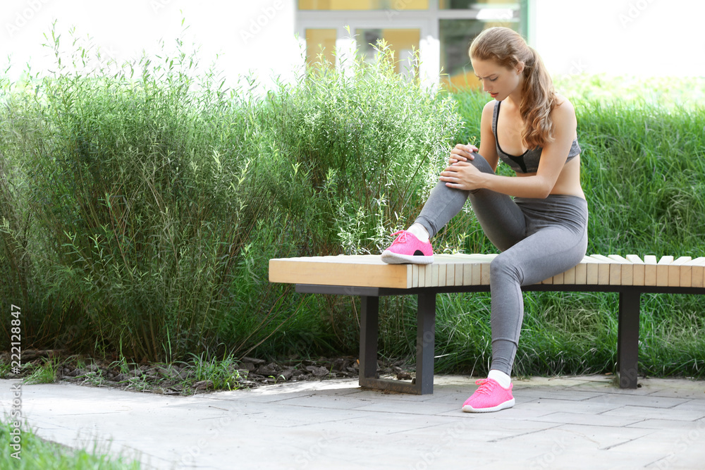 一名运动型年轻女子坐在公园的木长椅上膝盖疼痛