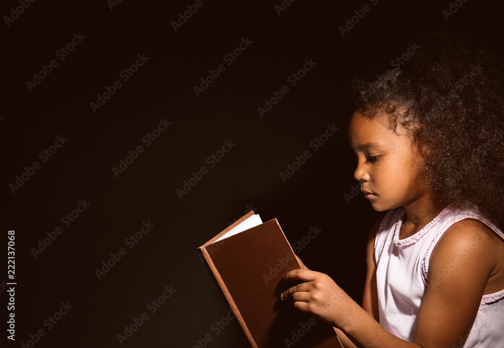 黑人小女孩在黑暗背景下看书