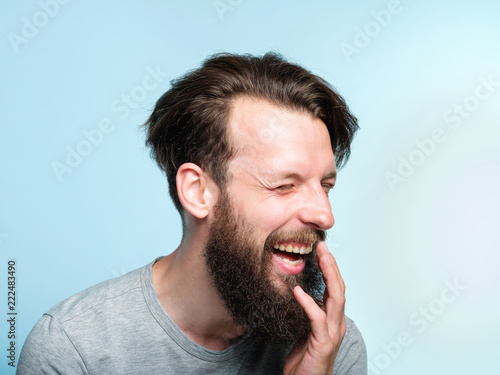 快乐的享受和笑声。咧嘴笑的男人。蓝色背景上一个留着胡子的年轻人的画像
