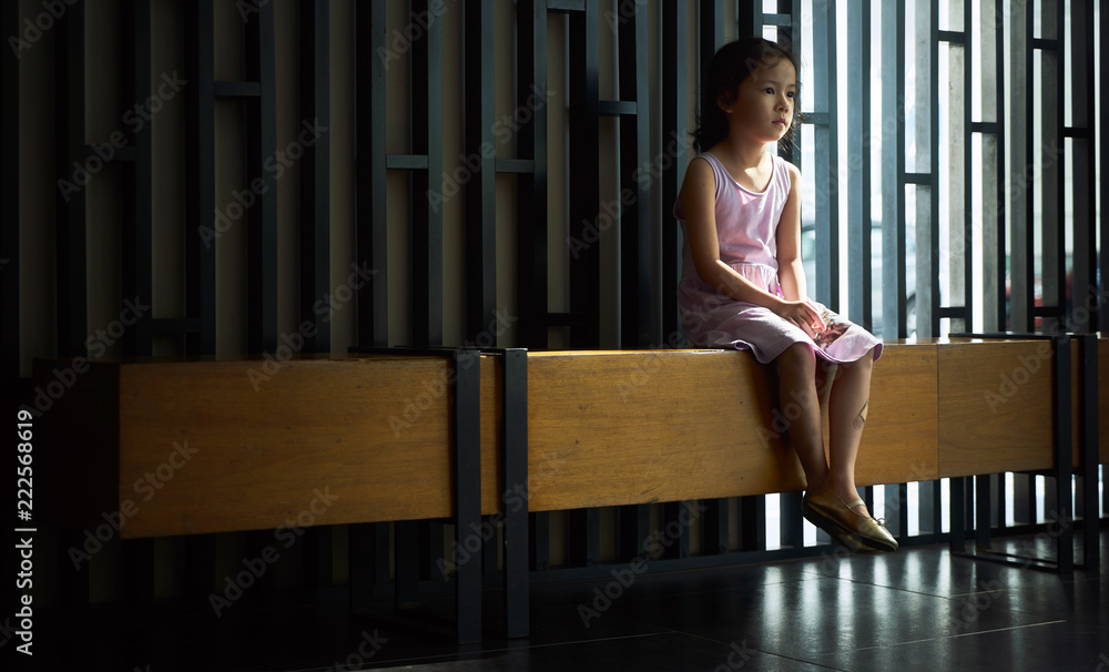 漂亮的亚洲小女孩孤独地坐在走廊的木制长椅子上。