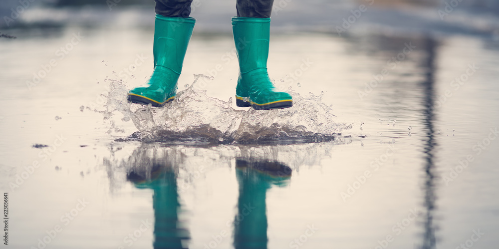 雨天孩子穿着雨靴在水坑里行走。夏天男孩在雨中