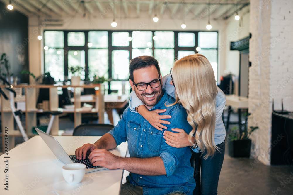 一对情侣在一家小型初创企业的现代化办公室拥抱。